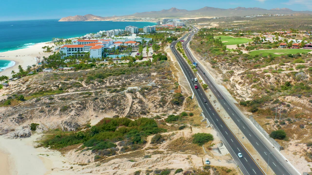 Highway traffic passes through sandy coastal terrain near beach, ocean, resorts, and hills.