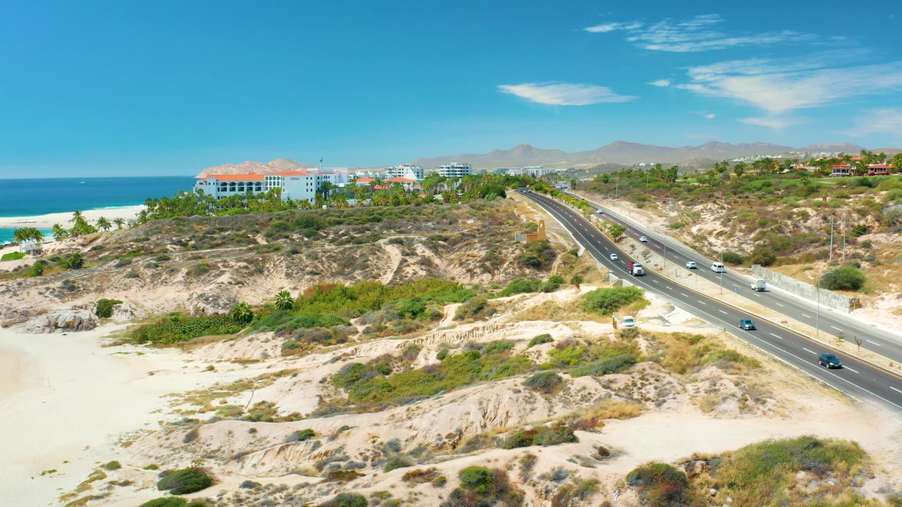 Elevated view of coastal highway, beach, ocean, scrubland, and hills.