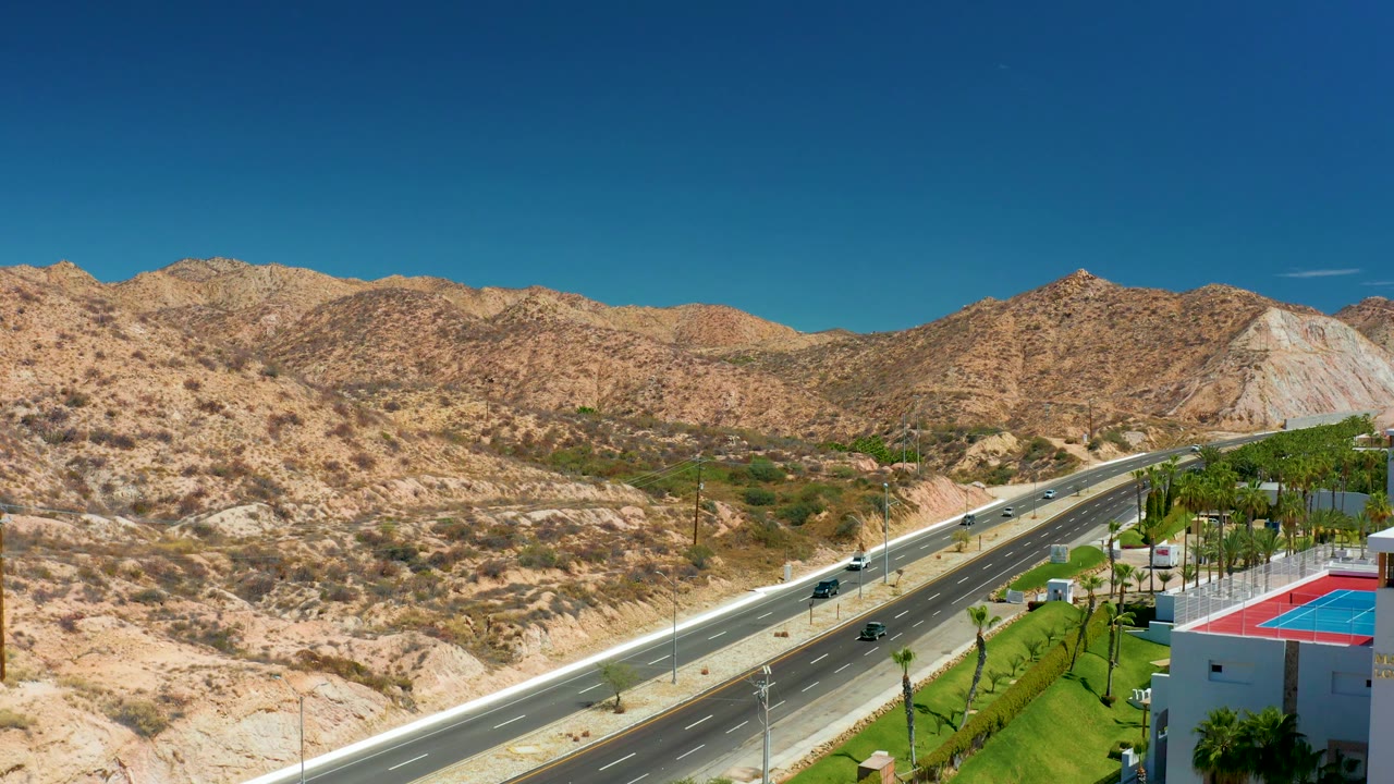 Wide road and desert hillside view with a building roof at the right edge.