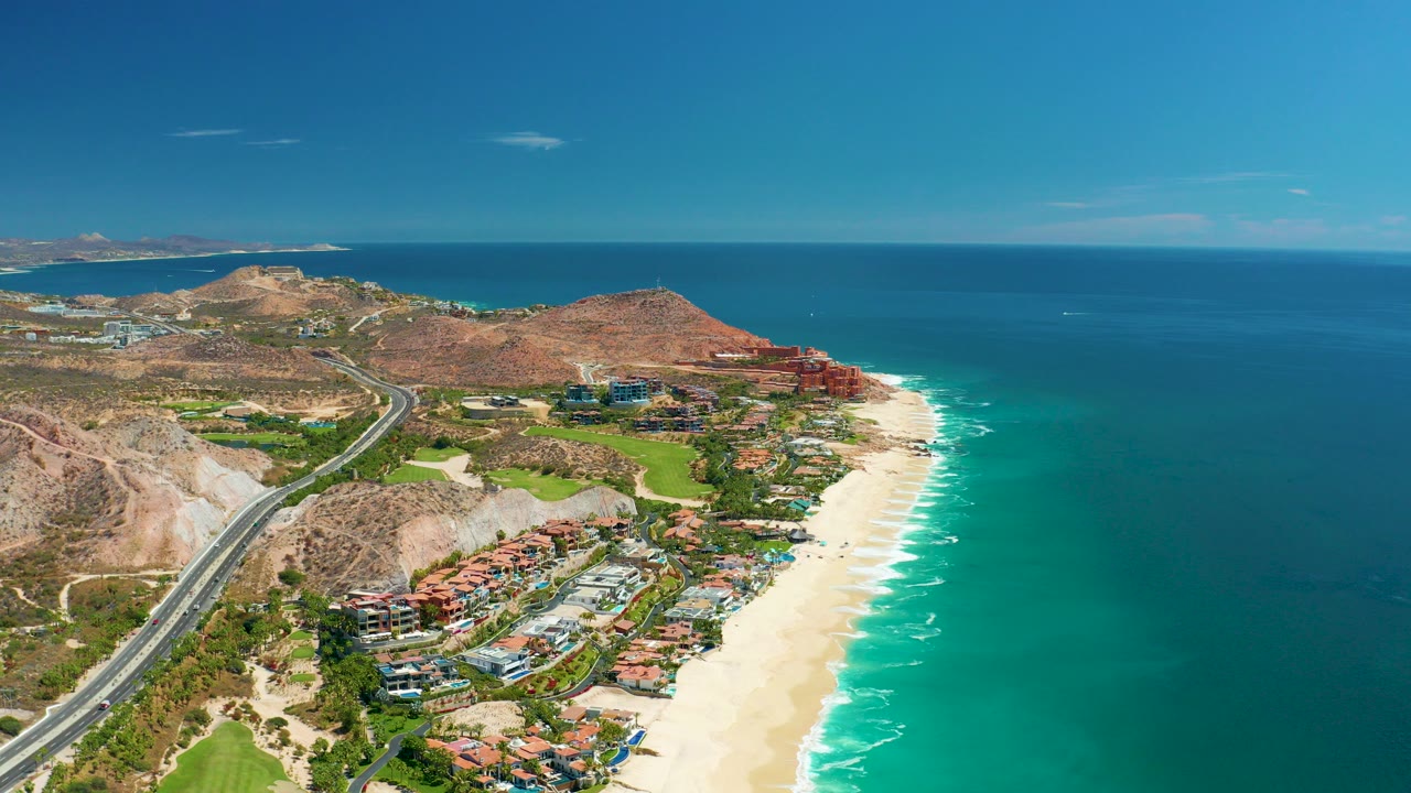 Aerial view of coastal highway, beach, ocean, hills, and buildings.