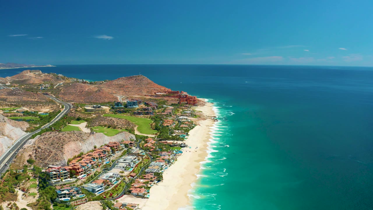 High aerial of road, green grounds, beach, surf, and ocean horizon