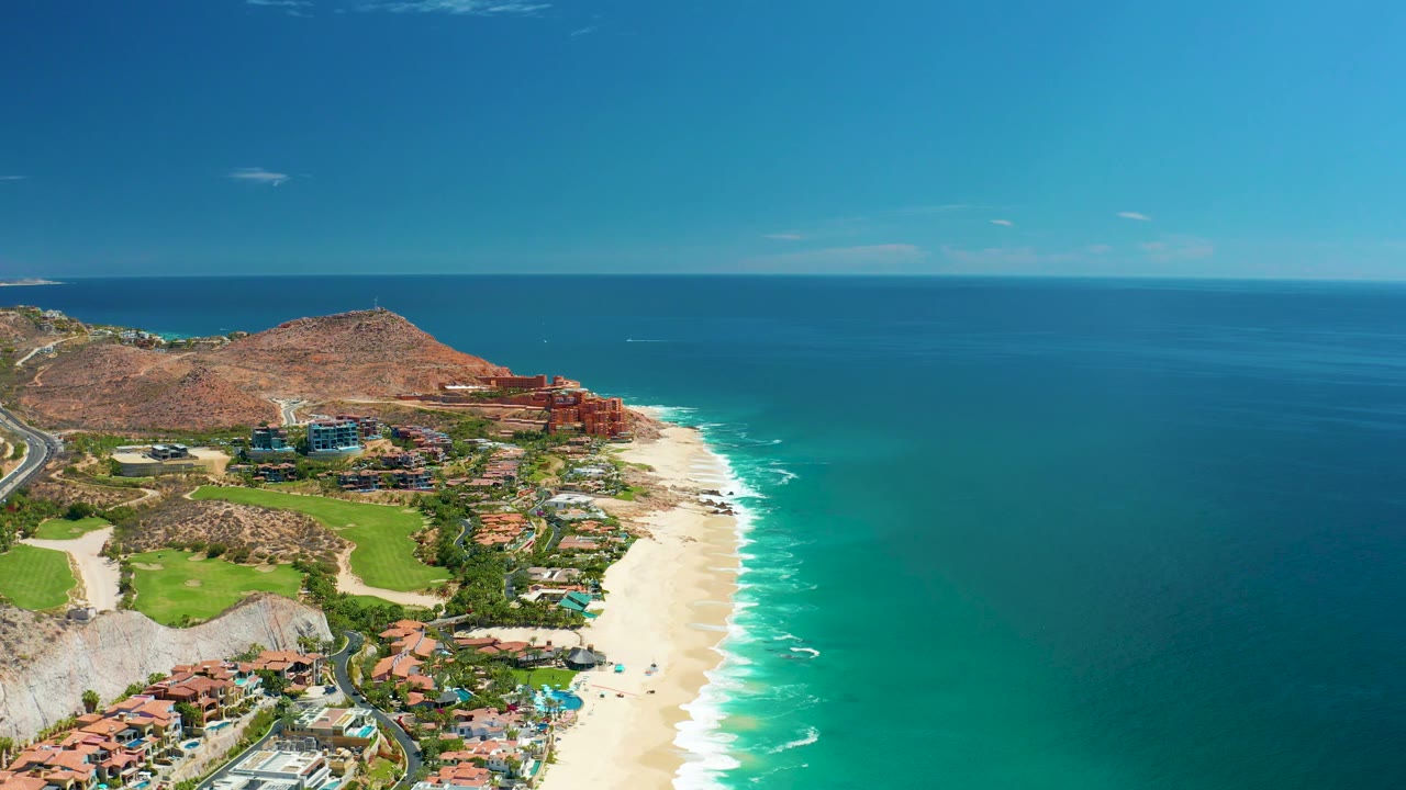 Coastal road and beach seen from above beside turquoise water.