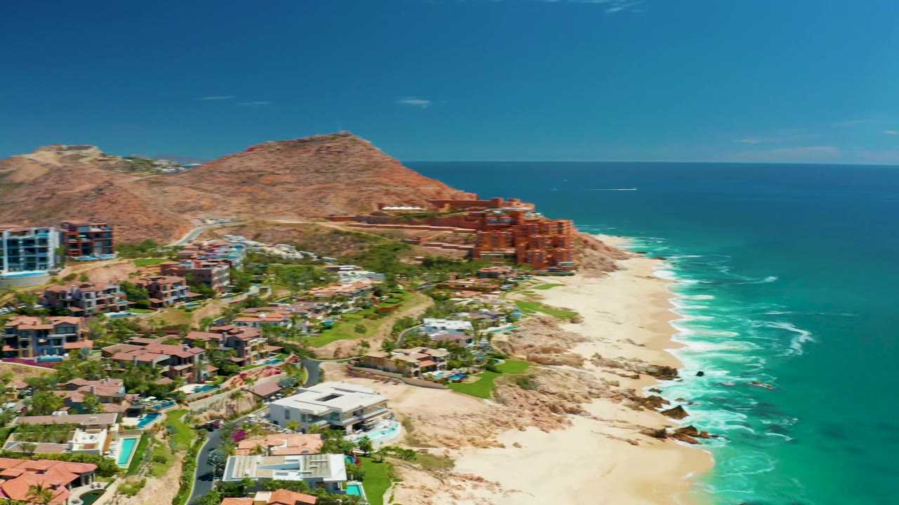 Coastal resort area with villas, beach, ocean, and mountains under clear sky.