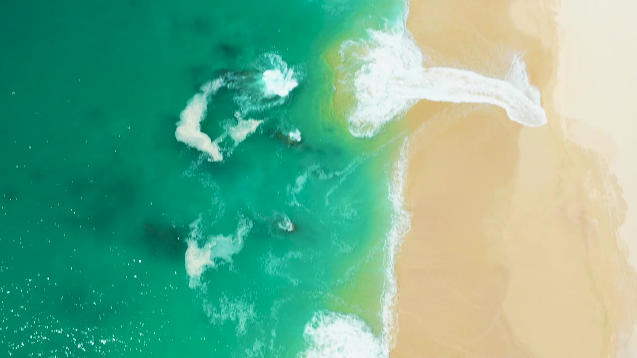 Overhead turquoise surf beside pale sand.