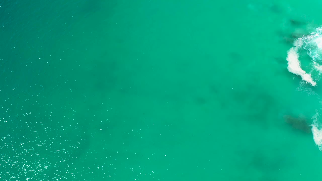 Clear turquoise water with a foamy wave along the right side.