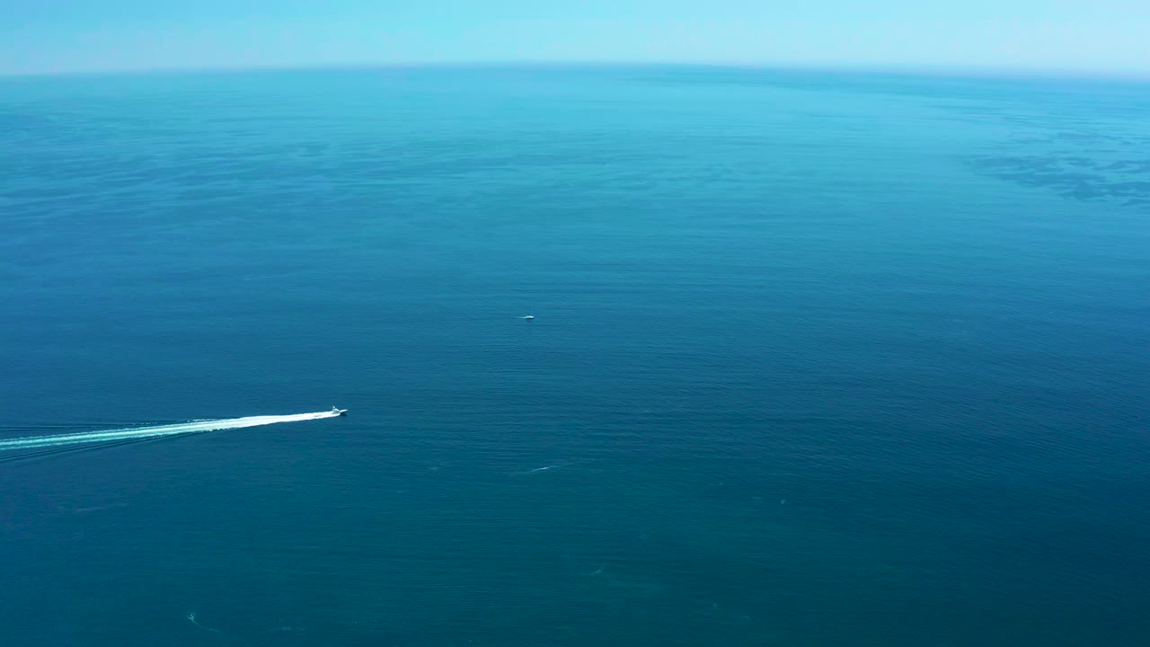 At Marquis Los Cabos in Mexico, a small speedboat runs across open blue water near the lower left of frame, leaving a white wake behind it, with no visible people.