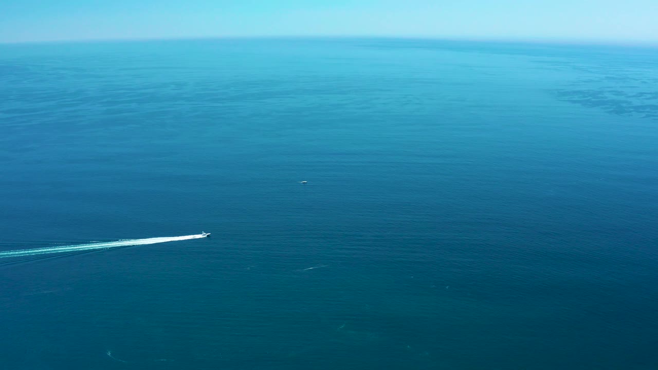 Speedboat near the left edge on open ocean under a clear sky.
