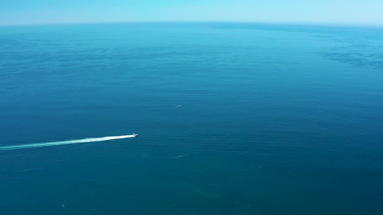At Marquis Los Cabos, Mexico, a small white speedboat enters the wide blue ocean frame from the left, trailing a long white wake with no visible people.