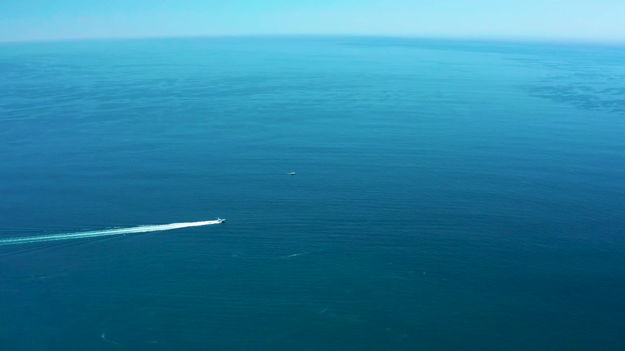 Speedboat farther right on calm ocean with white wake