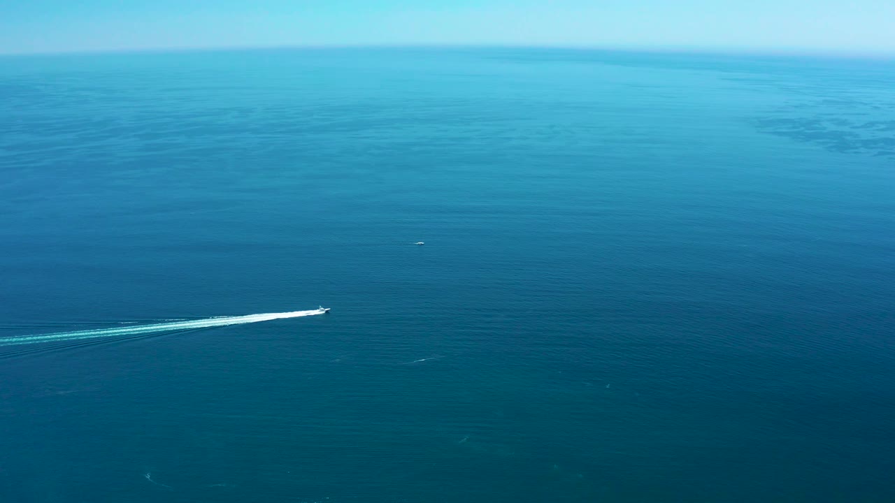 A small speedboat moves across the lower half of the blue ocean frame near Marquis Los Cabos, Mexico, with a pale trail and no visible people.