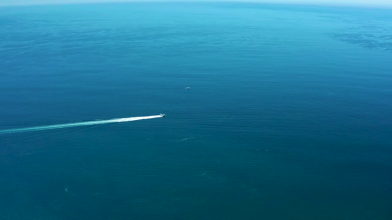 At Marquis Los Cabos, Mexico, the speedboat appears farther across the wide blue ocean, its white wake stretching diagonally behind it and no visible people in frame.