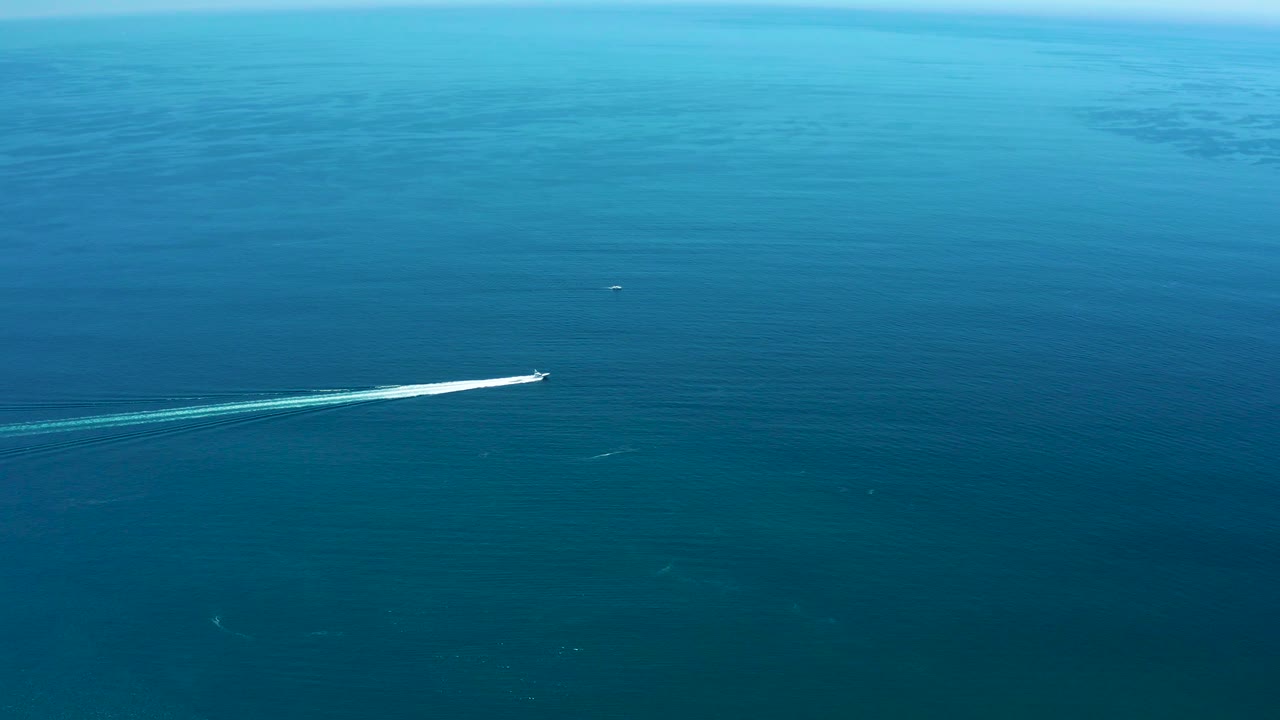 At Marquis Los Cabos, Mexico, the speedboat sits near the right side of the broad ocean frame, with a pale wake cutting across darker blue water and no visible people.