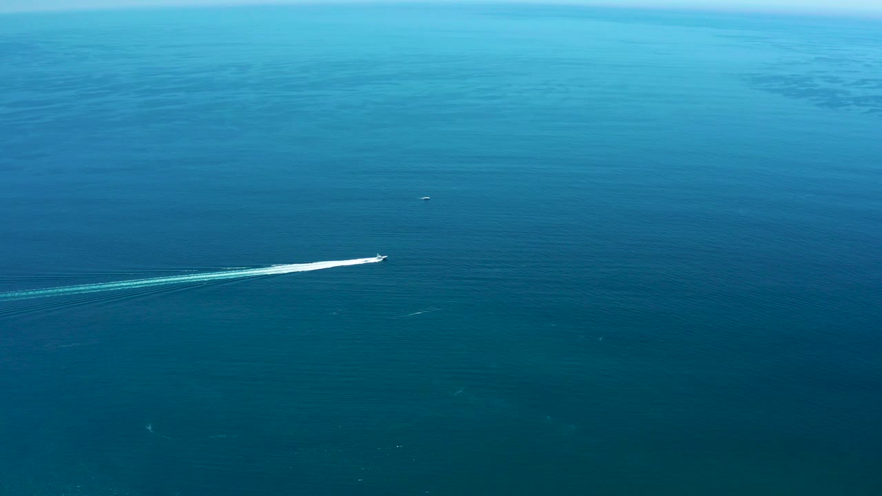 At Marquis Los Cabos, Mexico, the white speedboat is seen from an elevated angle over calm blue sea, with its wake bright against the darker water and no visible people.