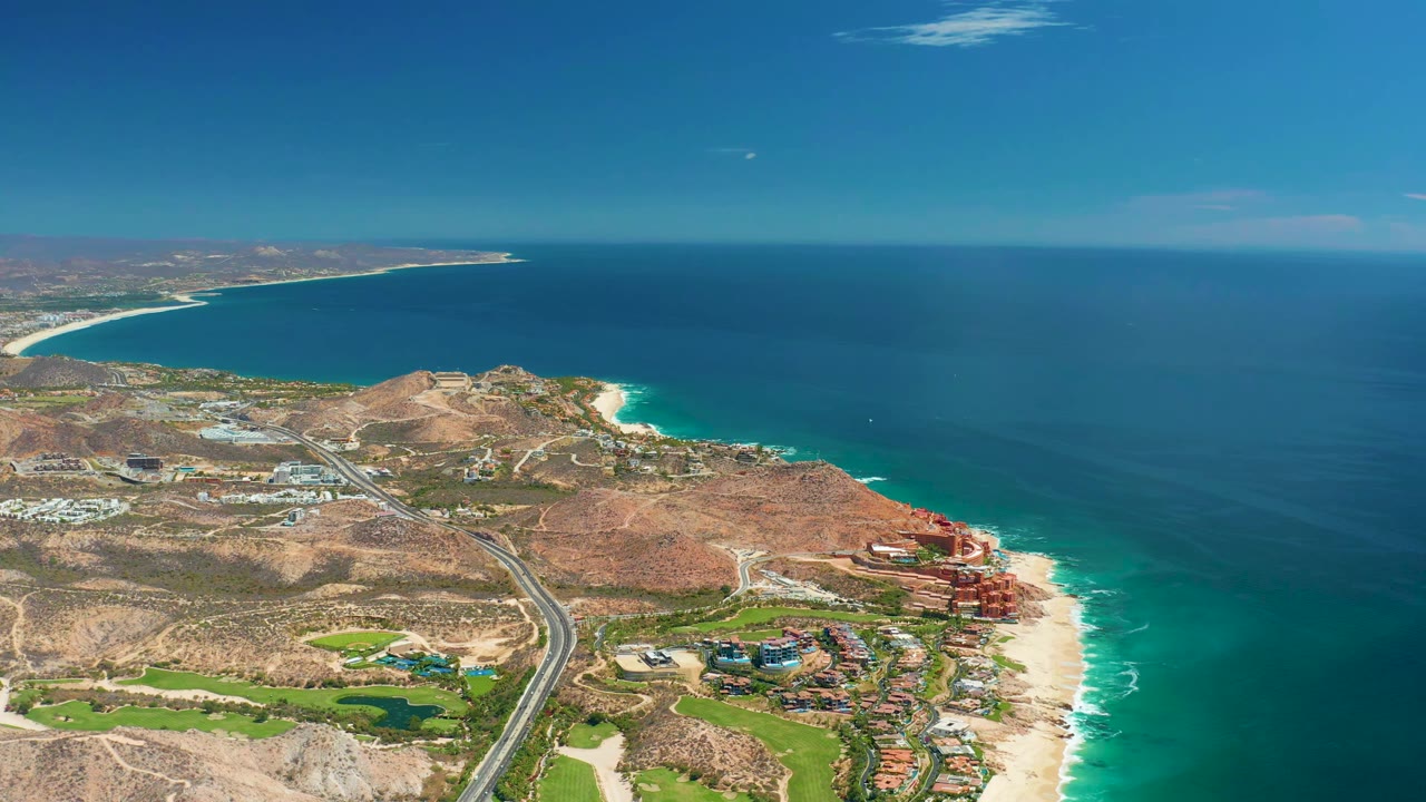 Drone view of ocean shoreline with highway and coastal development.