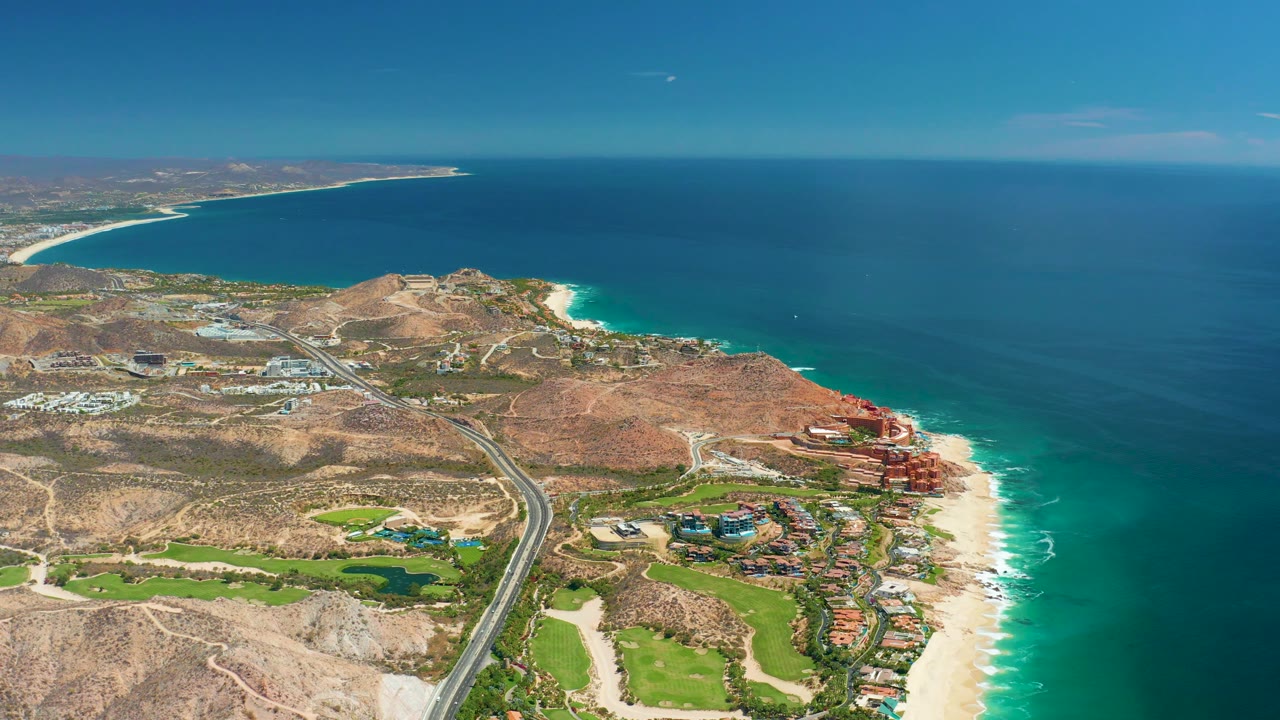 Coastal road and beach seen from above with ocean filling the right side.