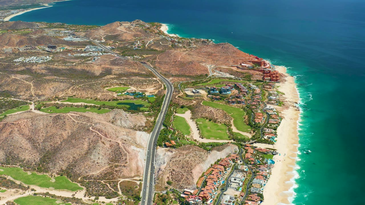 High aerial coastal view with road, hillside terrain, golf course, beach, and ocean.