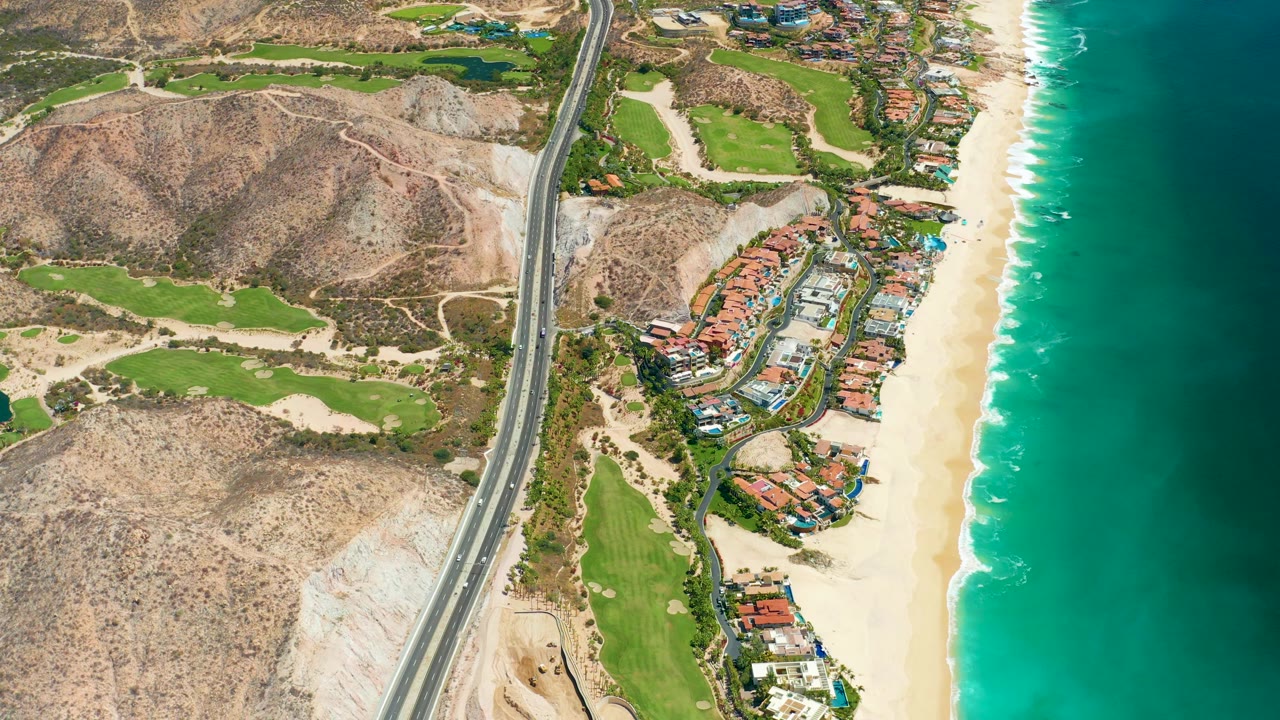 Aerial coastline with highway, green grounds, sand, and ocean