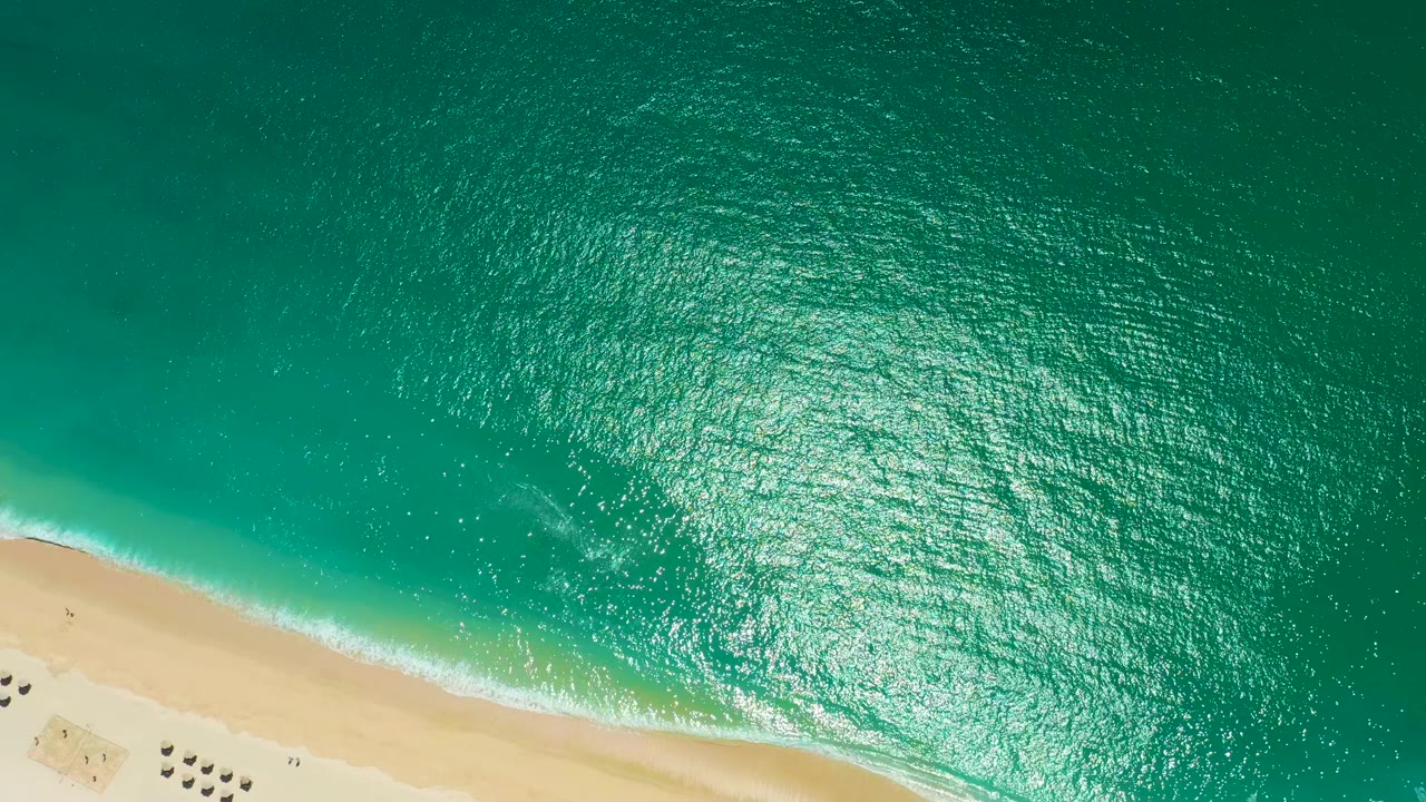 Top-down ocean ripples above a pale beach strip