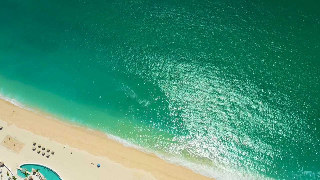 Aerial view of shimmering turquoise water and pale beach with umbrellas below.