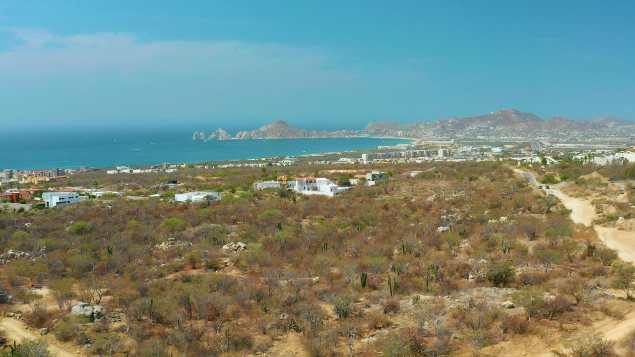 Coastal desert aerial with scrub foreground, road at right, ocean, and hazy hills.
