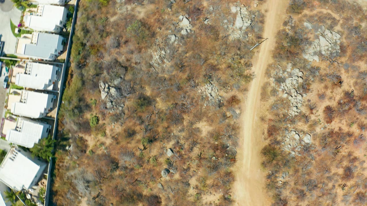 Dry land and dirt road beside a row of white buildings.
