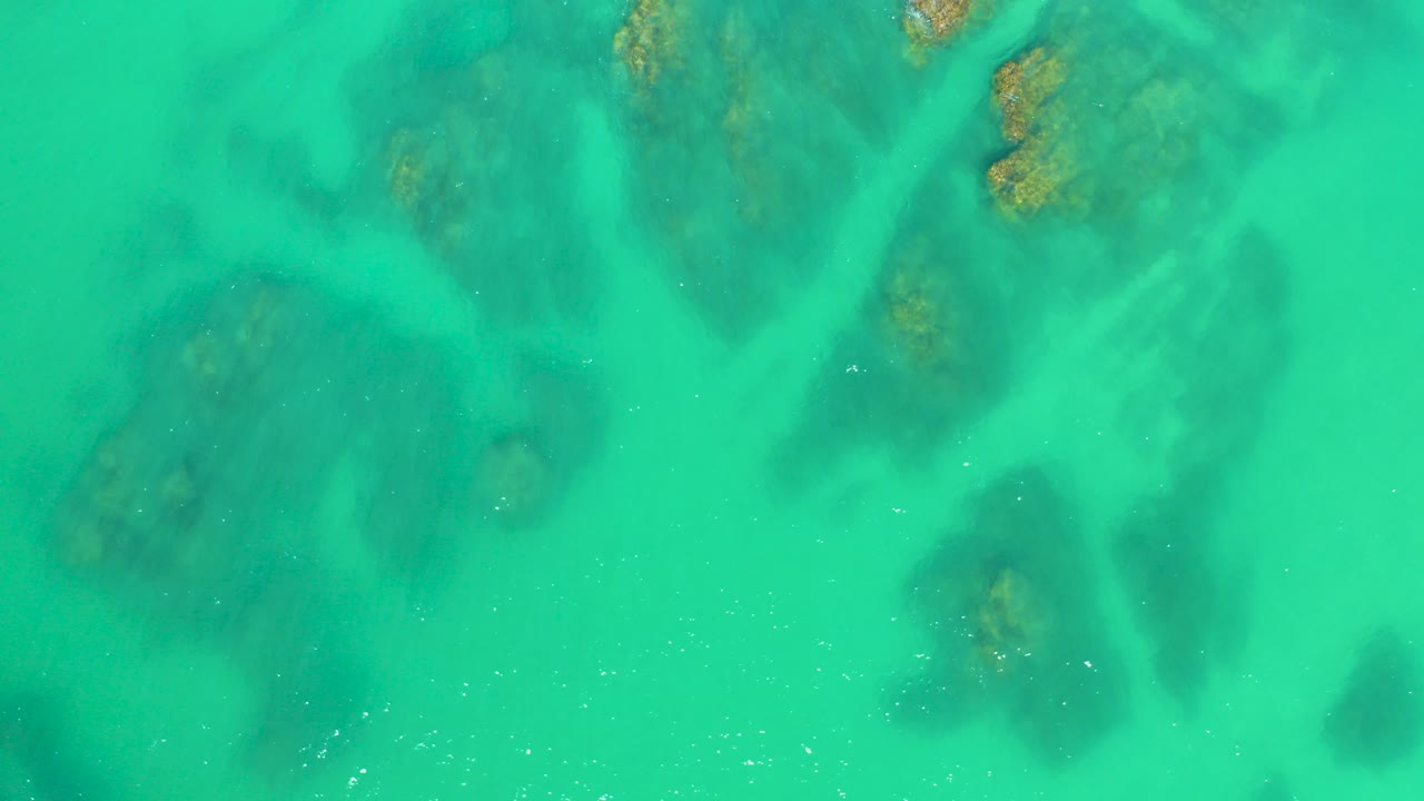 Turquoise shallow water over dark submerged rock formations.
