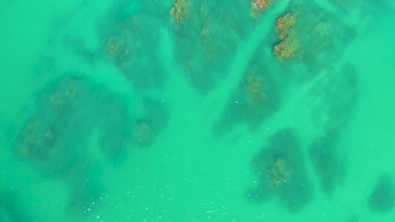 Clear water at Dreams Los Cabos reveals darker underwater rock shapes under a bright turquoise surface, with no visible people.