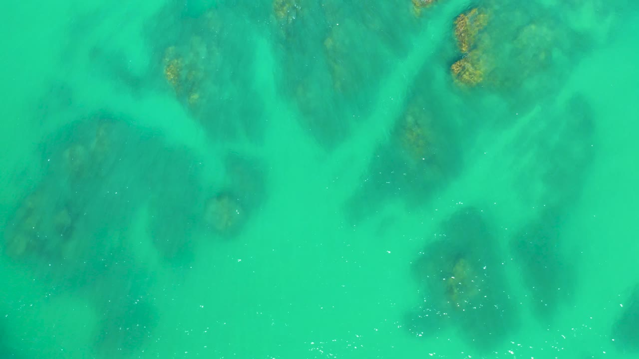 Top-down water detail at Dreams Los Cabos shows darker rocky patches beneath a smooth turquoise surface, with no visible people.