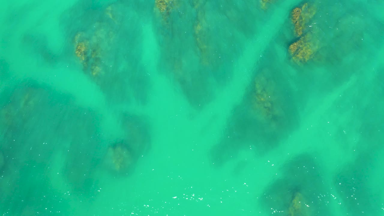Straight-down aerial frame at Dreams Los Cabos showing rippled turquoise water, mottled bottom texture, and no visible people.