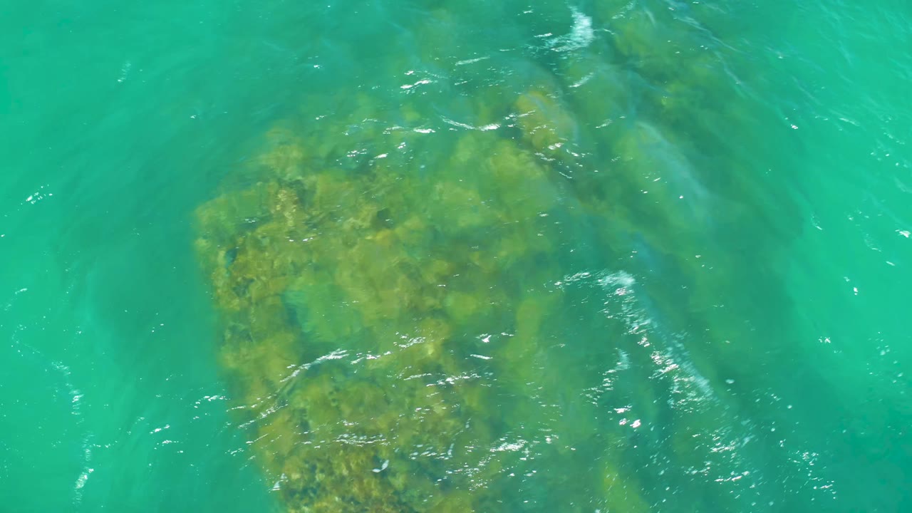 Clear turquoise water reveals a rocky seabed at Dreams Los Cabos, with the main rock mass centered lower in frame and no visible people.