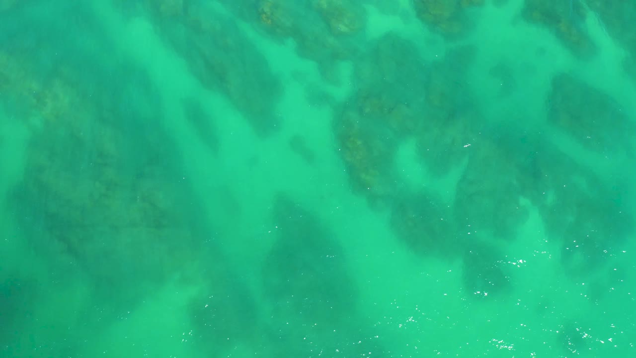 Overhead view of clear turquoise water above dark underwater rock formations at Dreams Los Cabos, with no visible people.
