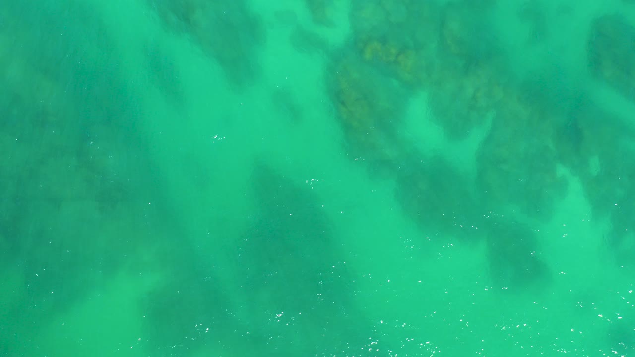 Overhead view of turquoise shallow water at Dreams Los Cabos with dark submerged rock shapes visible beneath the surface and no visible people.