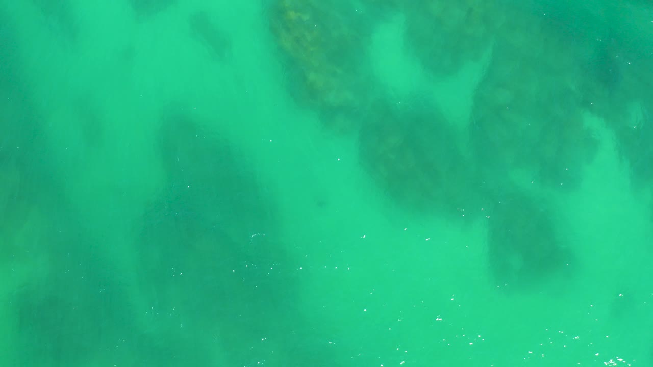 Turquoise shallow water over dark submerged rocks.