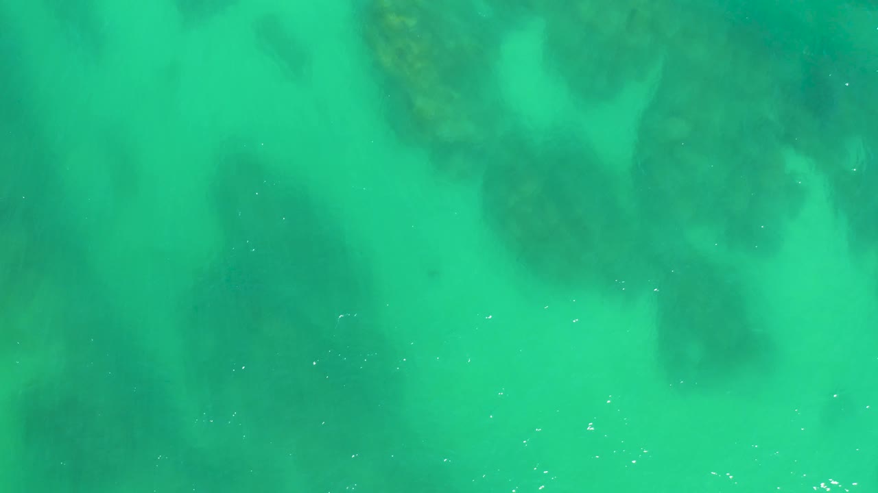 Clear green-turquoise water reveals broad dark rock patches beneath the surface at Dreams Los Cabos, with no visible people or shoreline.