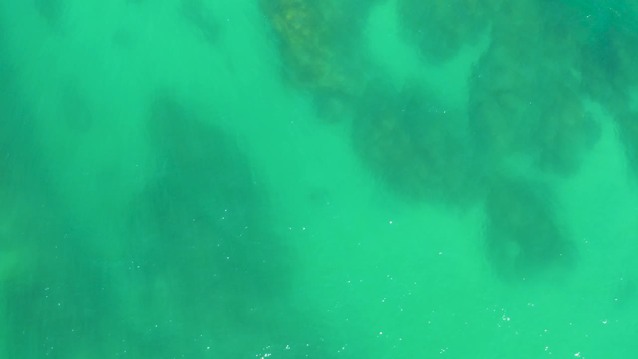 Aerial-style view of shallow turquoise water with darker submerged rocks concentrated near the top of the frame at Dreams Los Cabos, no visible people.
