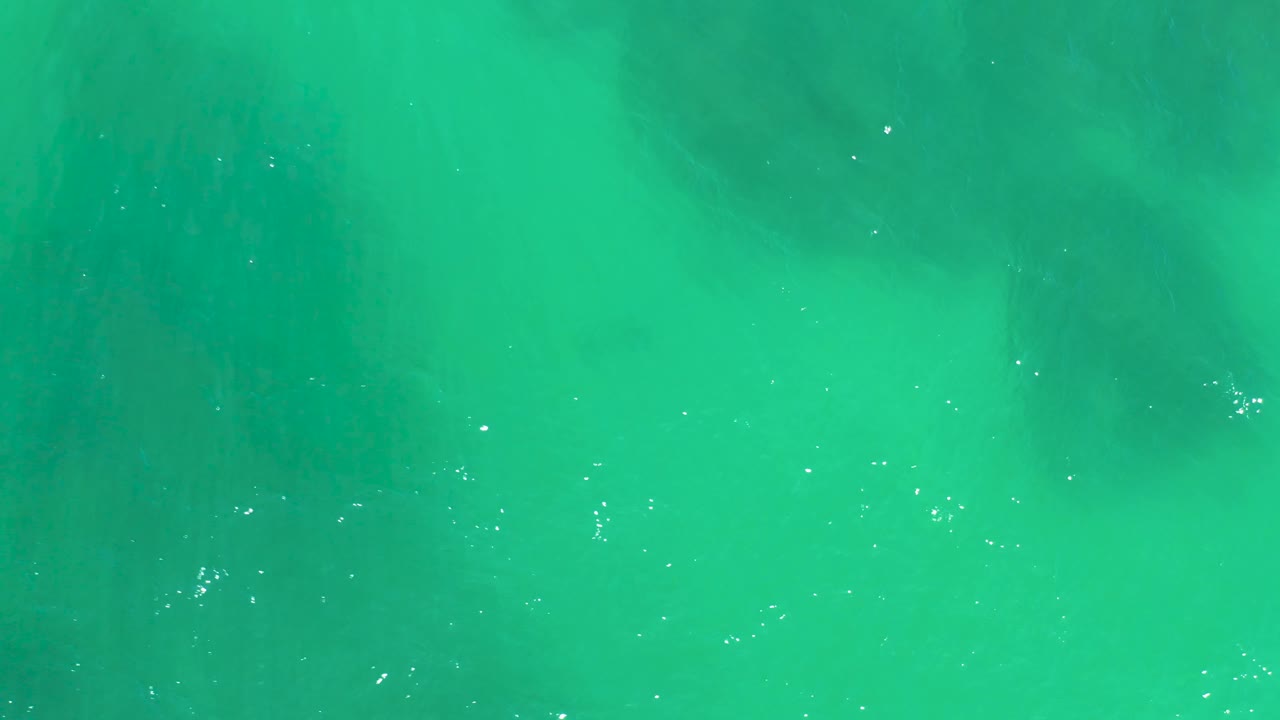 Clear green-blue ocean water at Dreams Los Cabos shows broad darker seabed shapes under the surface, small white highlights, and no visible people.