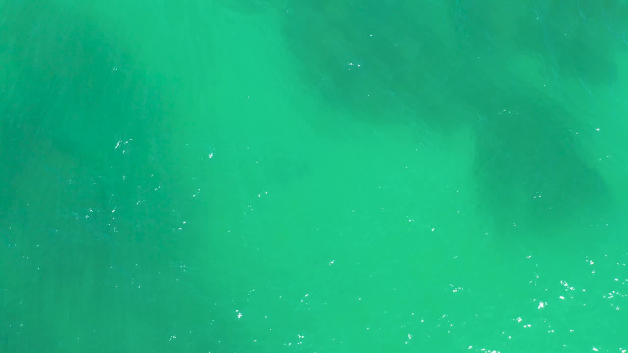 Bright turquoise water at Dreams Los Cabos fills the frame with soft shadowy underwater rock shapes and scattered surface sparkle, with no visible people.