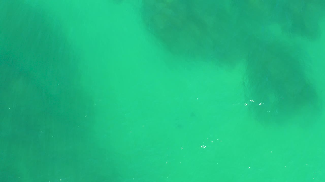 Clear turquoise water at Dreams Los Cabos with dark submerged rock shapes near the upper frame and no visible people.