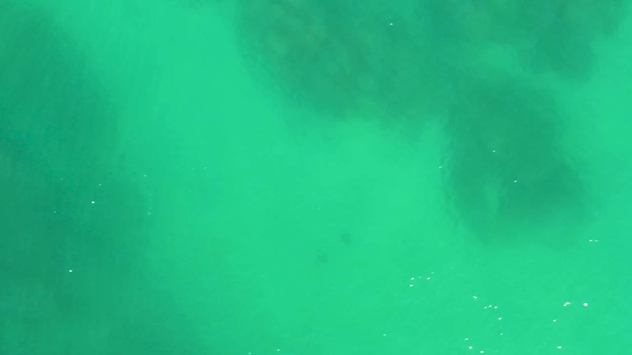 Turquoise shallow water at Dreams Los Cabos contains faint white bubbles and darker submerged patches, with no visible people.