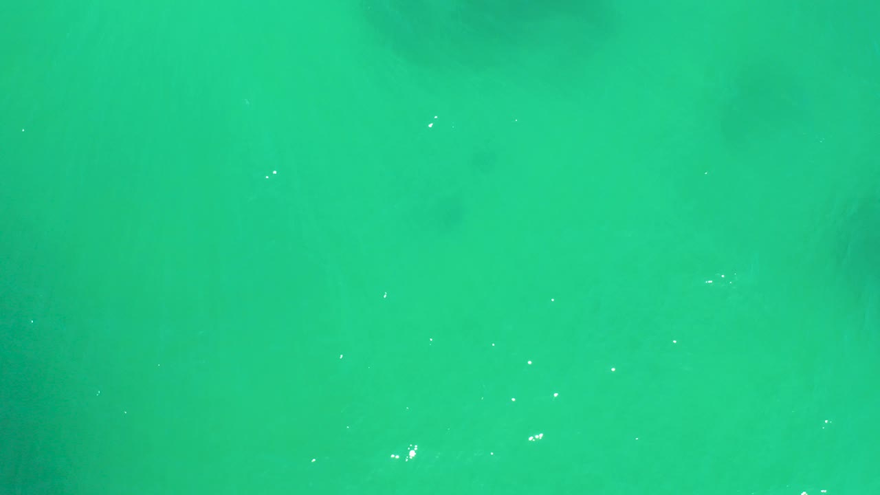 Overhead turquoise ocean water at Dreams Los Cabos with faint darker underwater features and small light specks, no visible people.