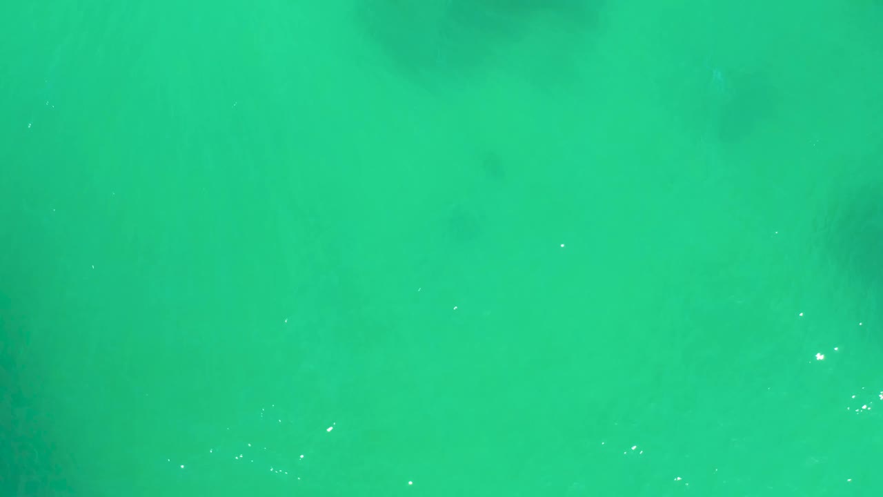 Turquoise sea surface in Baja California Sur with soft darker underwater forms visible beneath the water and no visible people.