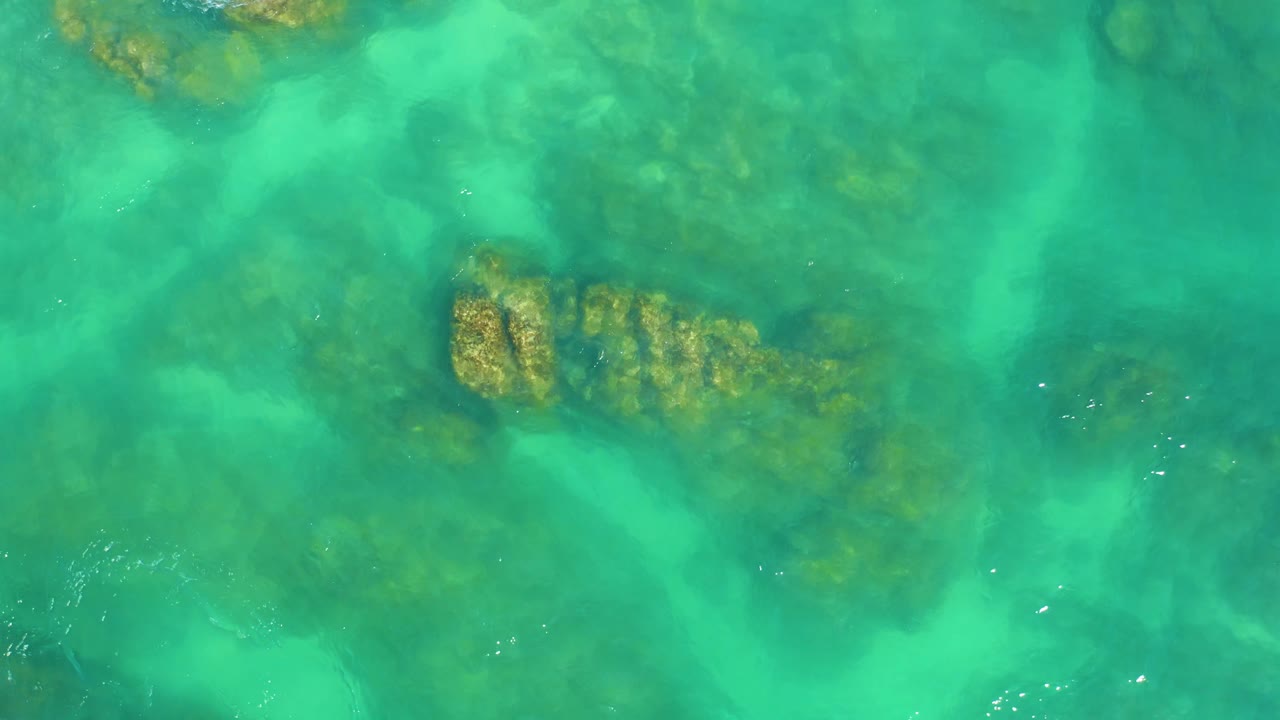 Clear green-blue water reveals a submerged rock and coral patch slightly left of center at Dreams Los Cabos, with no visible people.