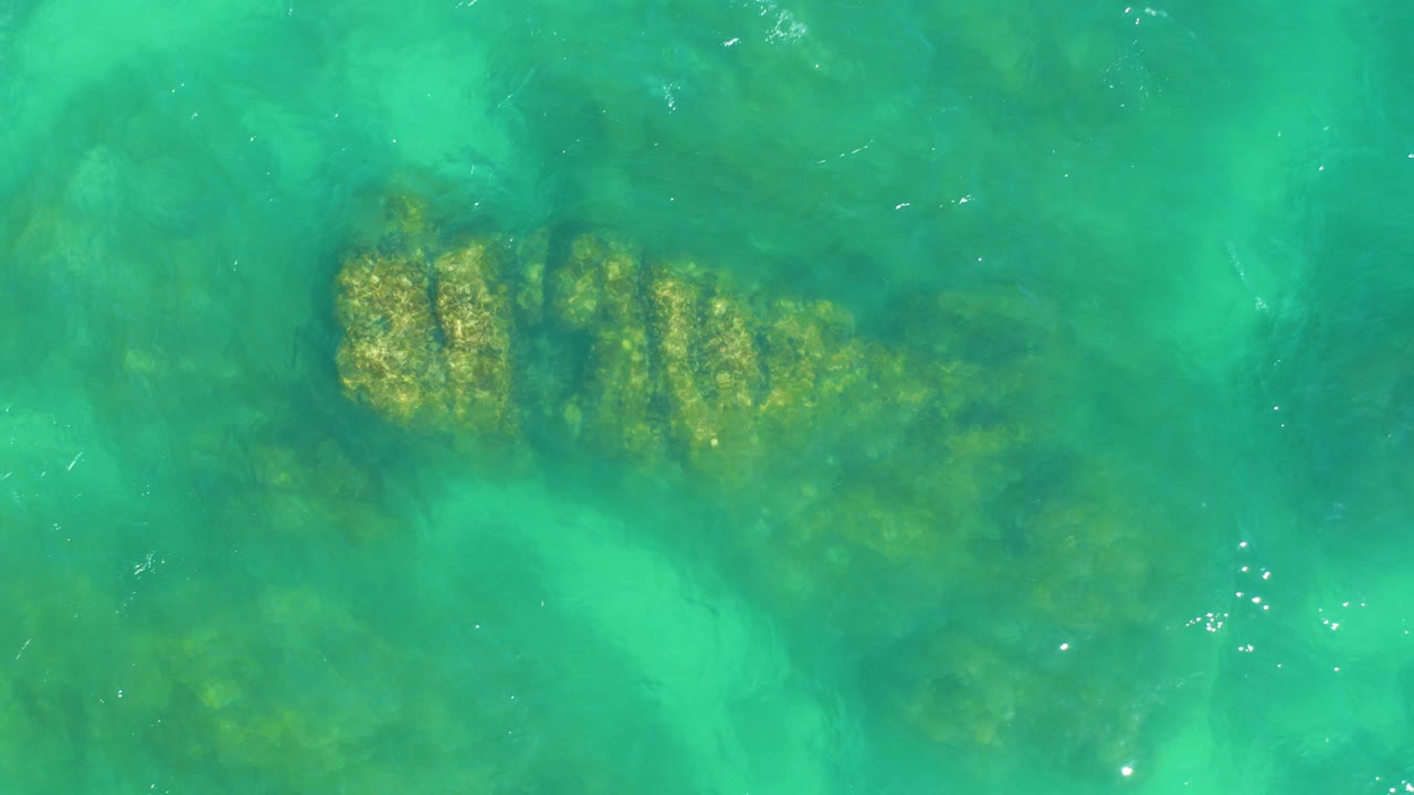 At Dreams Los Cabos, turquoise water reveals a long submerged rocky coral formation near the upper half of frame, with no visible people.