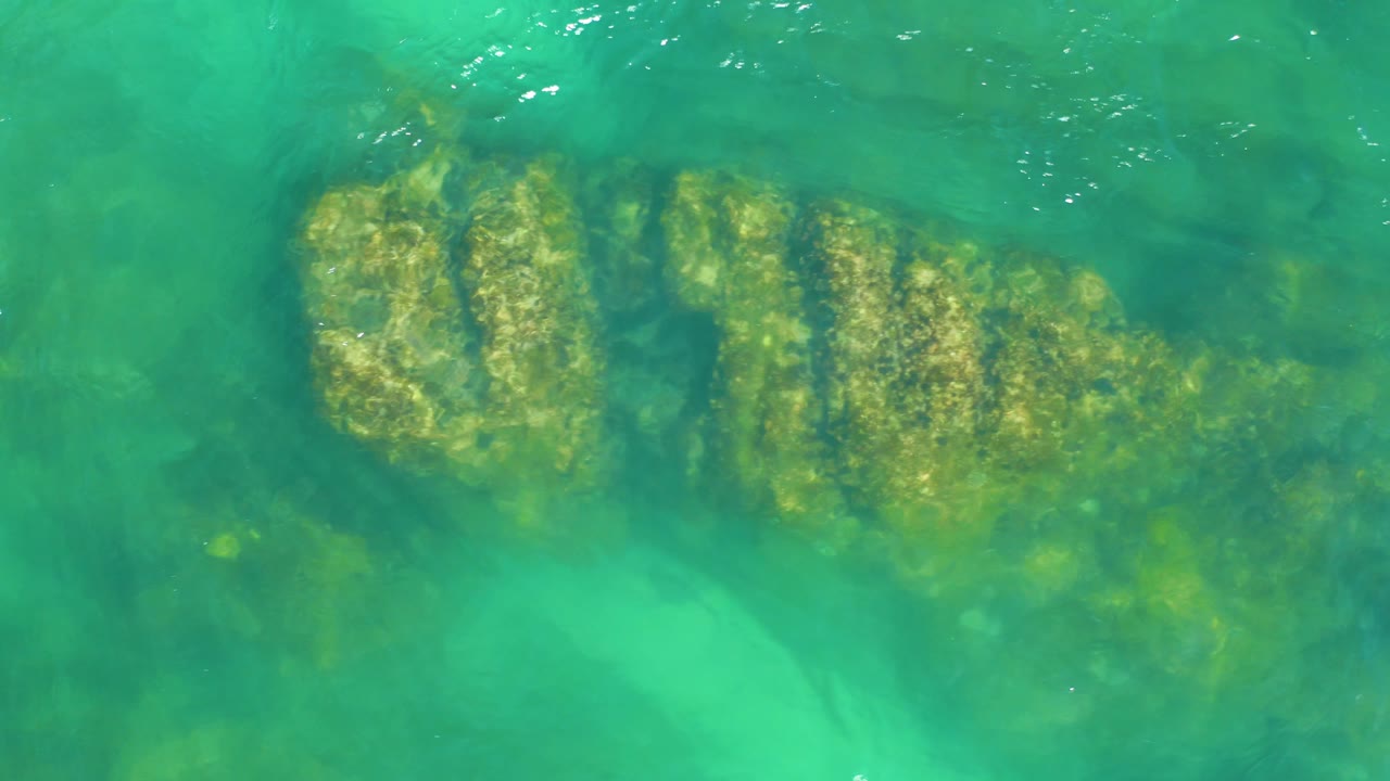 Overhead view at Dreams Los Cabos showing submerged rock ridges through turquoise water, with brighter shallow patches and no visible people.