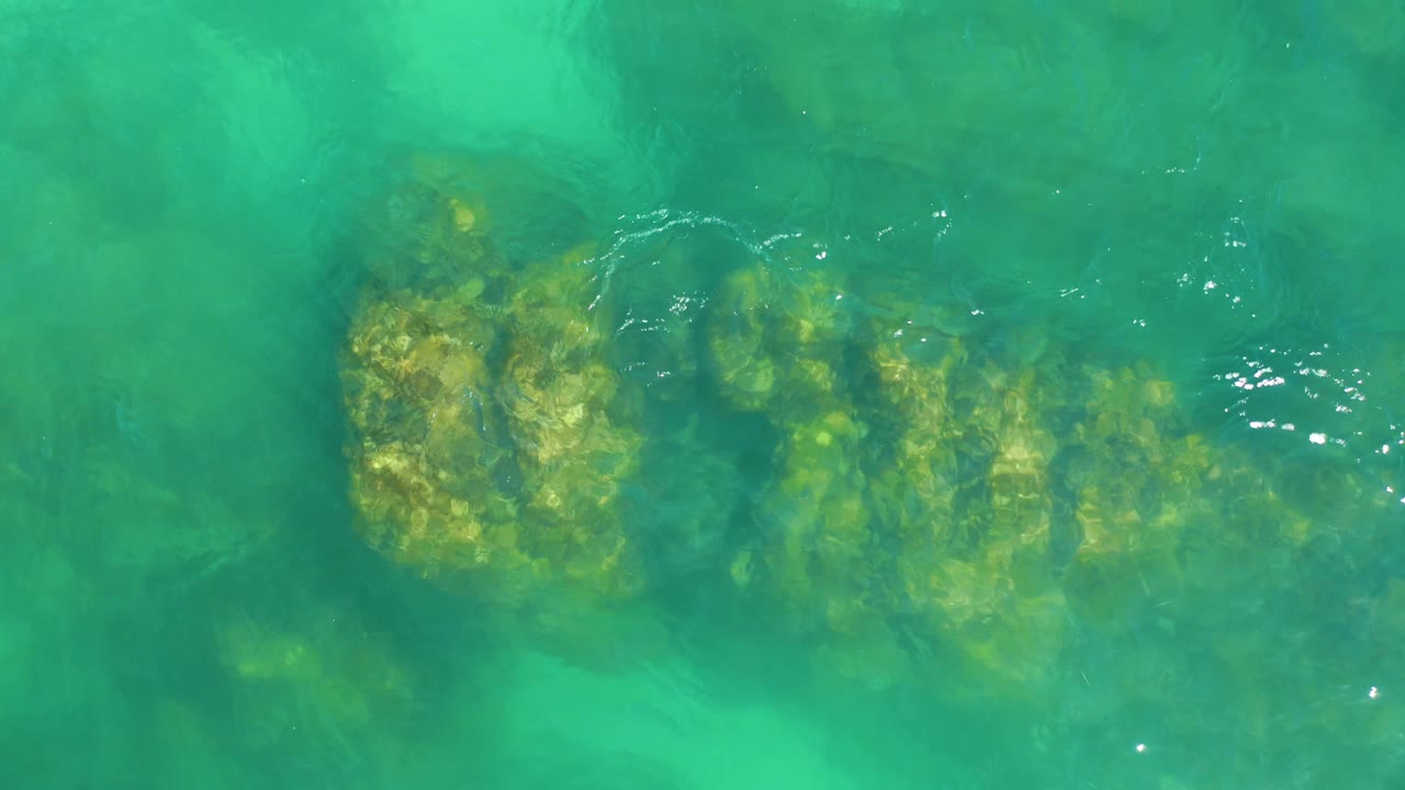A submerged rock cluster sits under clear turquoise ocean water at Dreams Los Cabos, with lighter green patches around it and no visible people.
