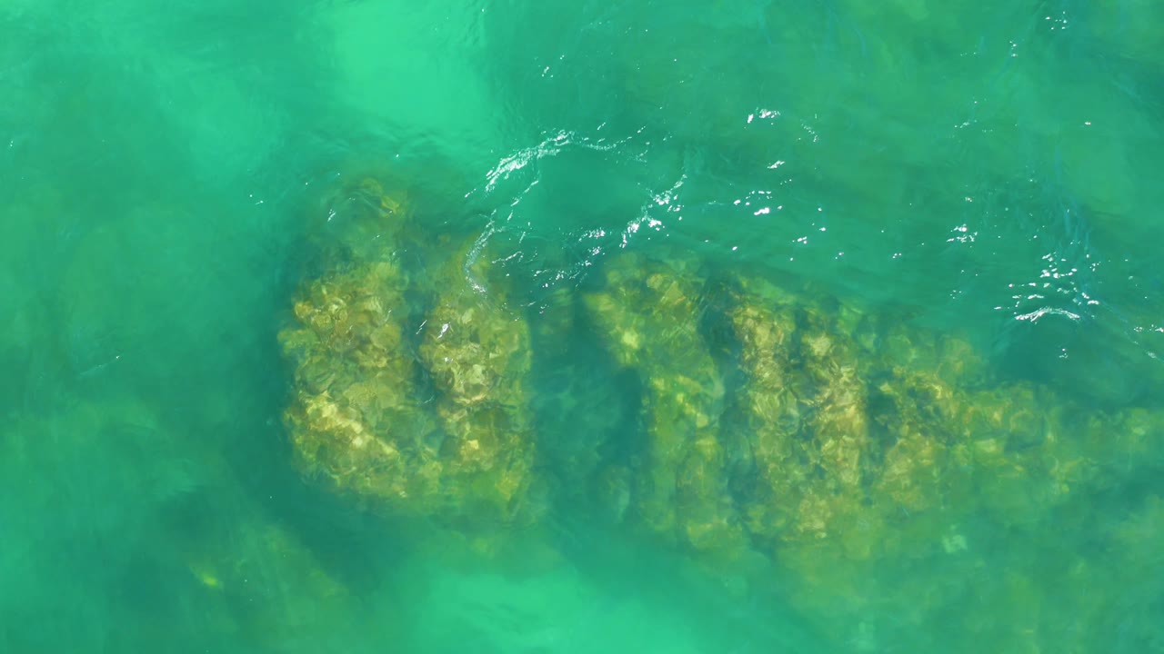 Clear green water passes over a broad underwater rock shape at Dreams Los Cabos, with soft surface distortion and no visible people.
