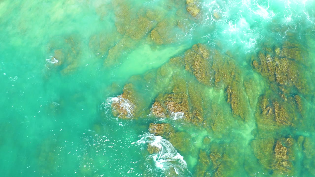 Overhead turquoise water with submerged rocks and small white surf patches.