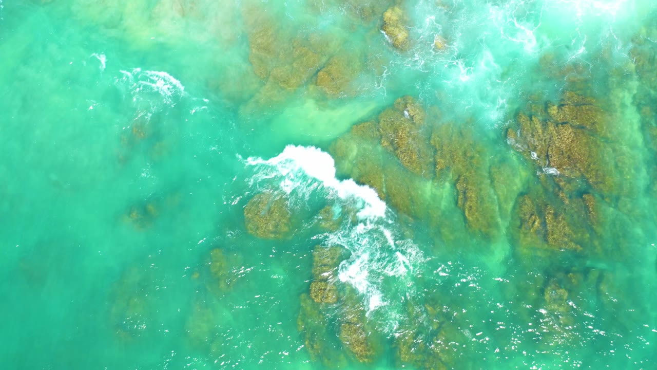 The 0:03 overhead frame at Dreams Los Cabos shows a larger white wave patch crossing brown submerged rocks in clear turquoise water, with no visible people or vessels.