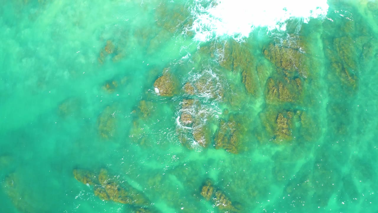At Dreams Los Cabos, submerged rocks sit beneath green-turquoise water while the white foam thins near the upper edge and no visible people appear.