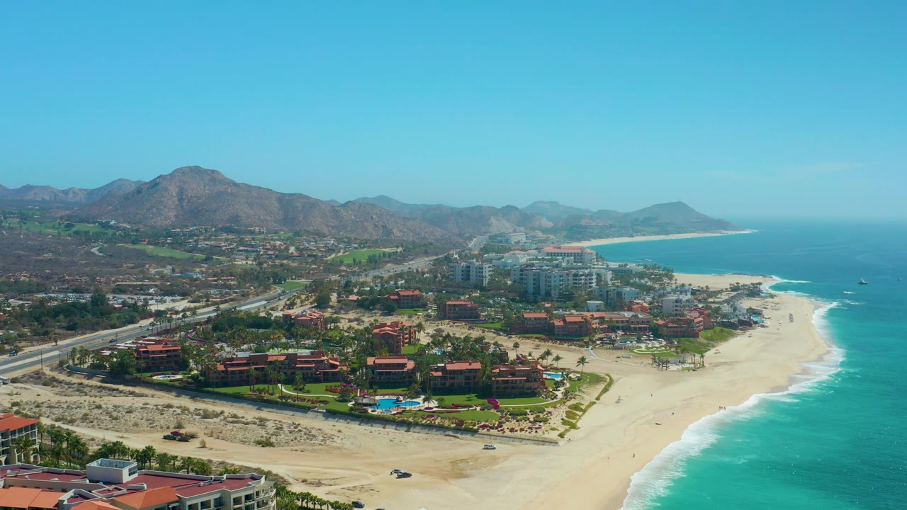 Aerial coastline view with highway, resort grounds, beach, and surf.